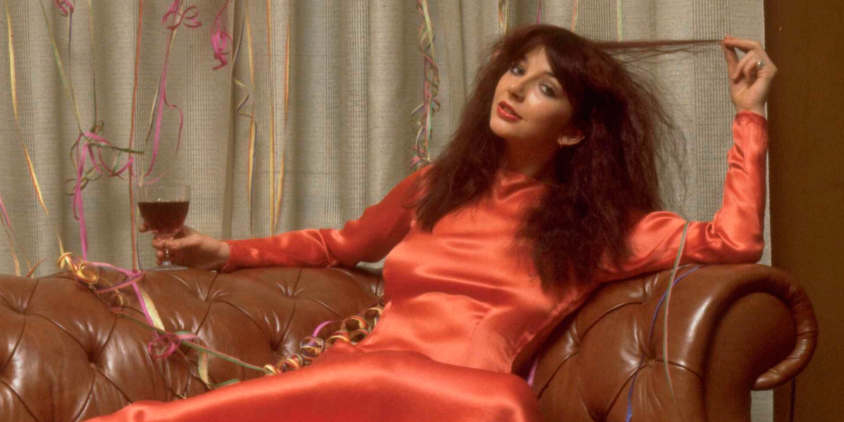 Kate Bush lounging on a sofa with a glass of something