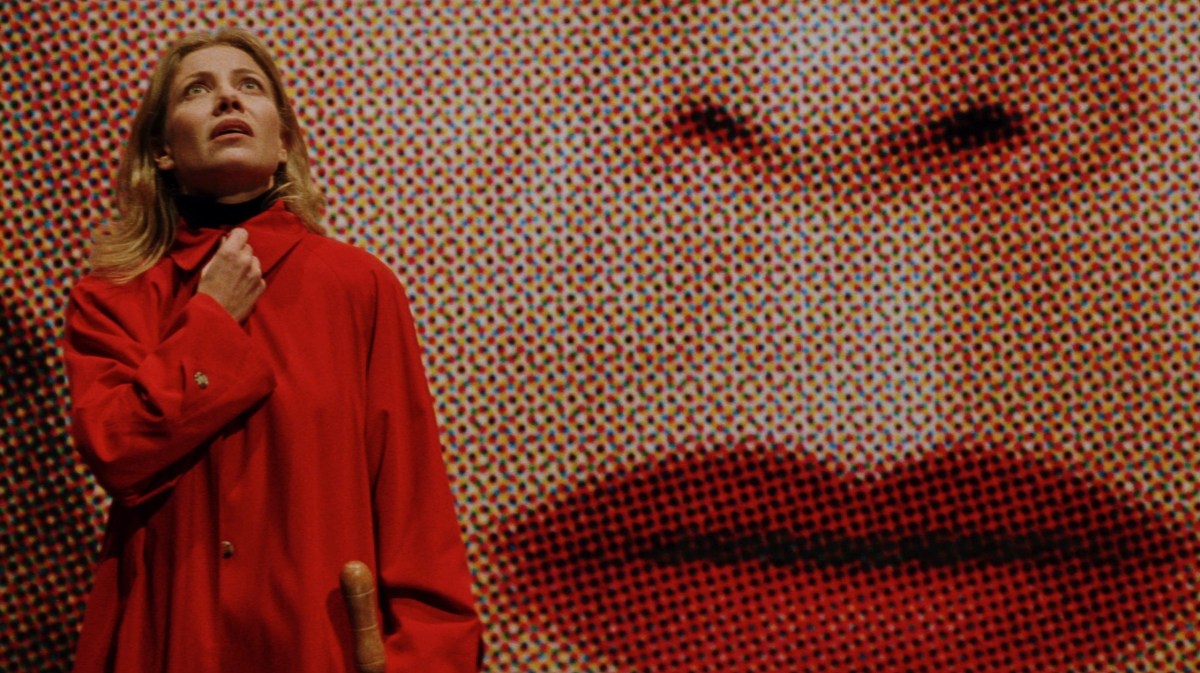 A woman in red stands in front of an ad with the face of another woman in close up