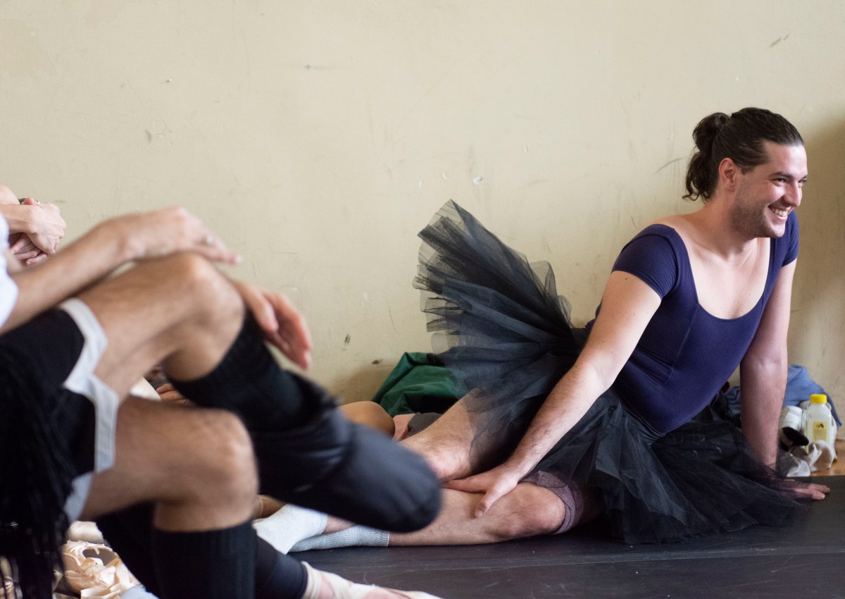 Andrea Fabbri smiles and stretches in a black tutu on the floor.