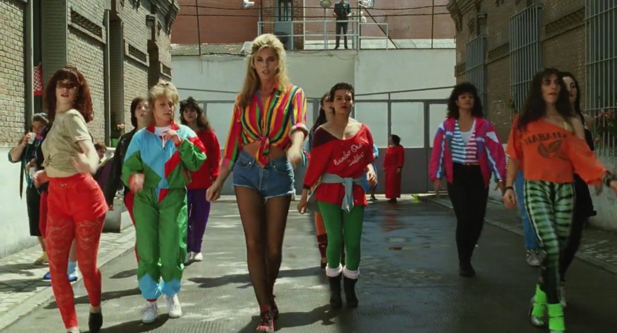 Bibiana Fernandez in a tied up shirt and jean shorts leads a group of woman in a dance in a jailyard.