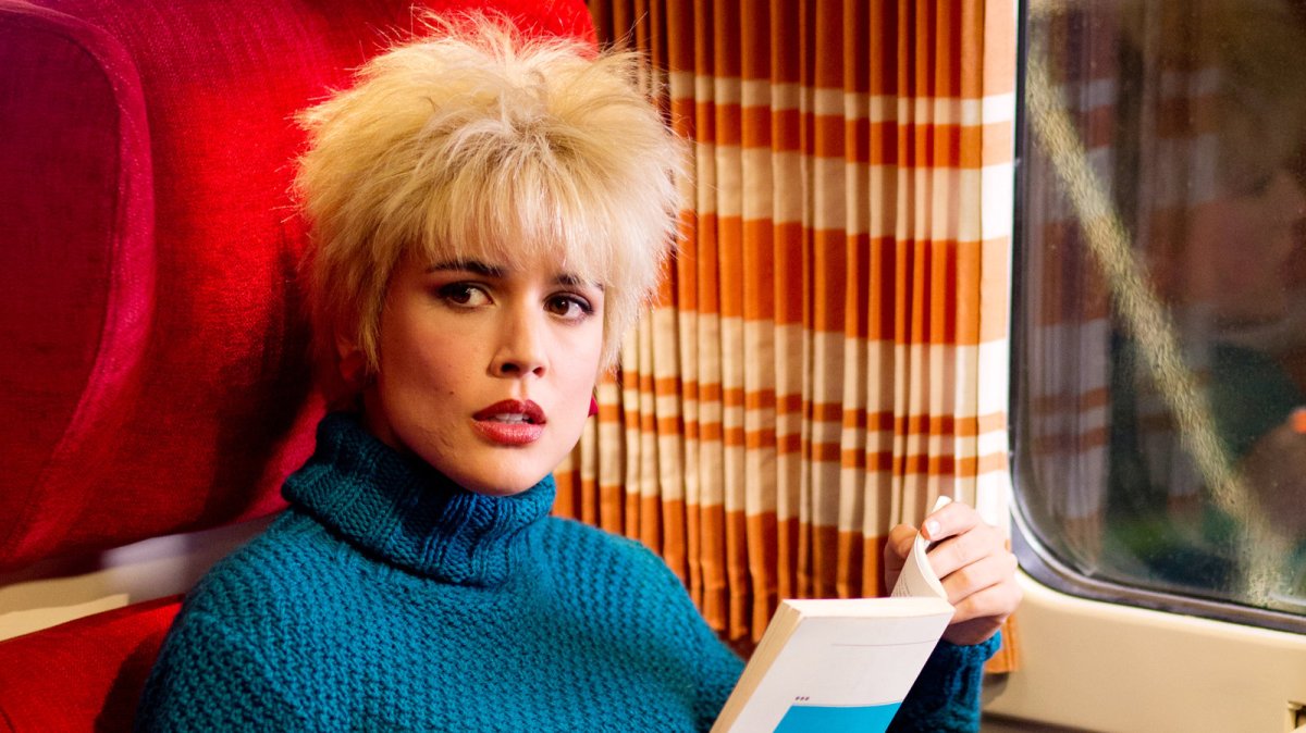 A woman in a blue sweater reads a book on a train.