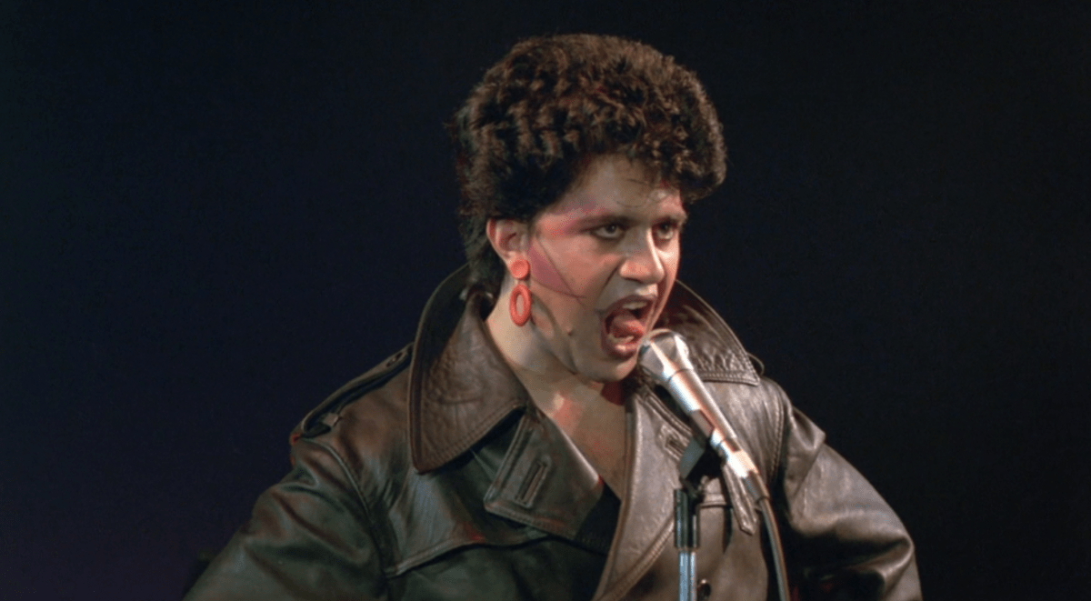 A young Pedro Almodóvar sings on stage in a leather jacket and femme punk makeup.