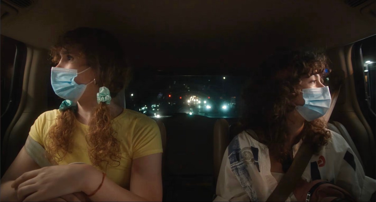 Theda Hammel and Amy Zimmer sit in the backseat of a car with masks on looking out opposite windows in Stress Positions.