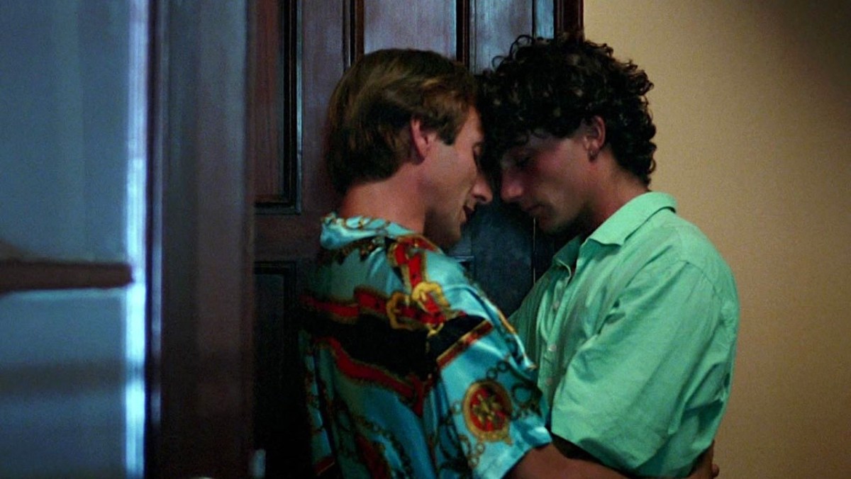 Every Pedro Almodóvar movie ranked: An older man and a younger man both in colorful shirts embrace by a door.