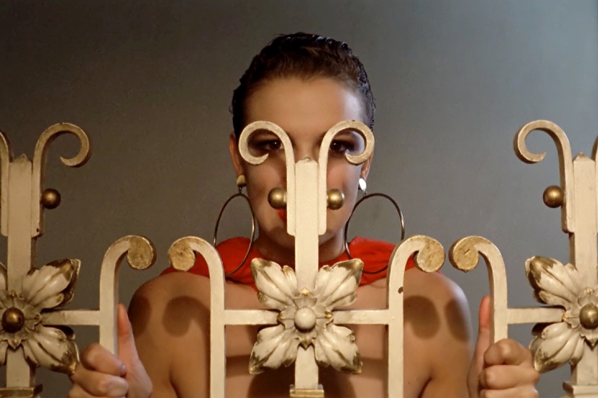 A woman frames her eyes in the loops of a gold metal gate.