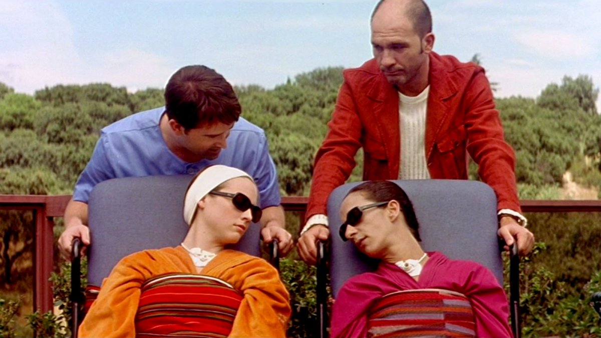 Two men hover over two unconscious women in sunglasses.