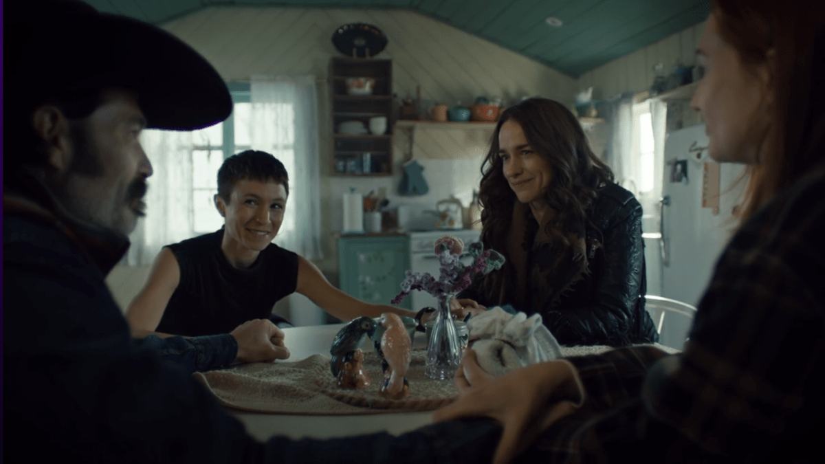 The main characters of Wynonna Earp sit around  a table smiling.