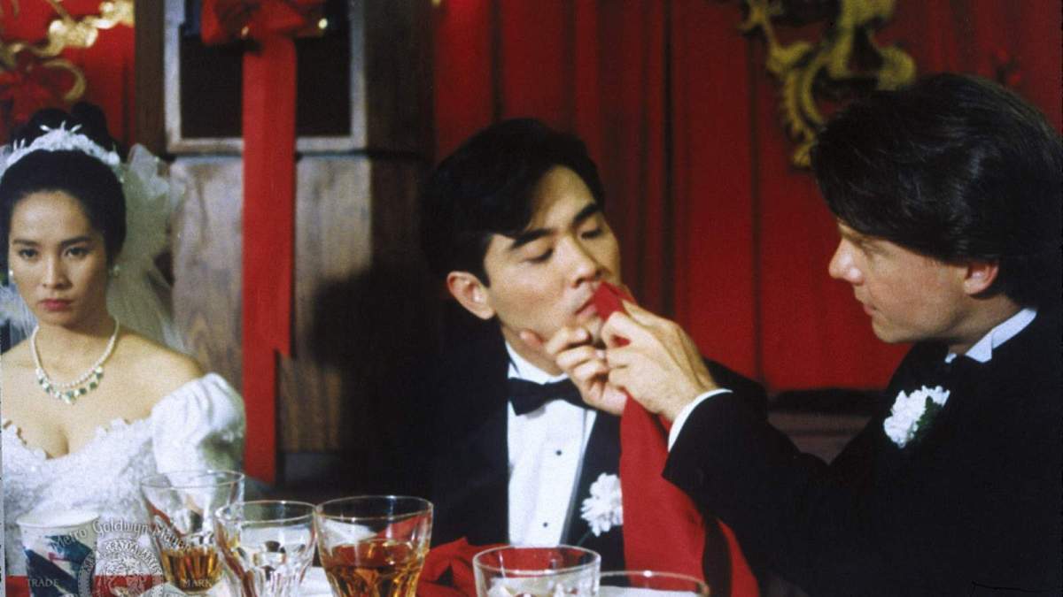 A white man wipes the lips of a Taiwanese groom sitting next to his Taiwanese bride.