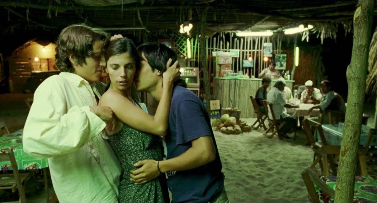 Two teen boys dance with an older women in the glow of a small restaurant's light. 