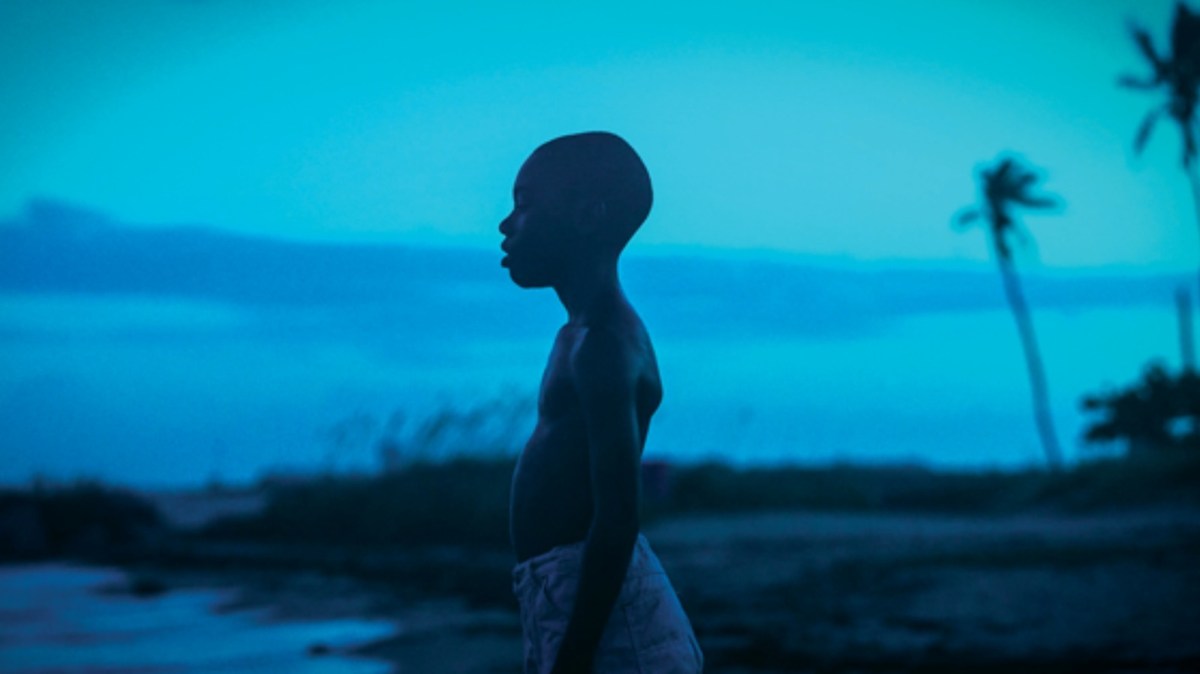 A boy looks out at the ocean in dark blue light.