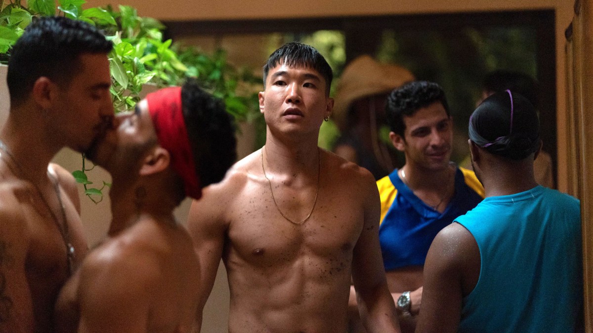 Joel Kim Booster walks through a gay party while shirtless.