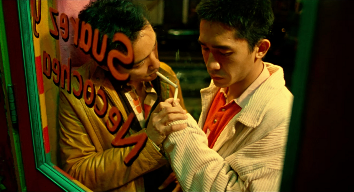 Tony Leung Chiu-wai and Leslie Cheung light each other's cigarettes leaning against a window.