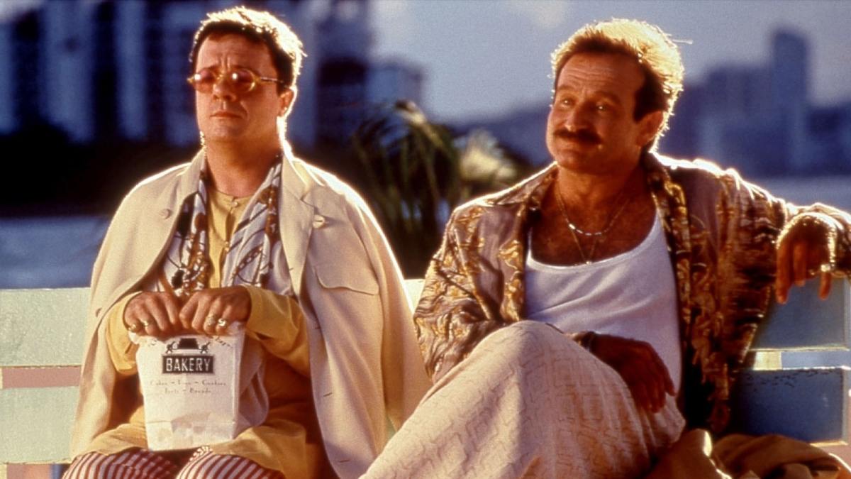 Nathan Lane and Robin Williams sit side by side in flamboyant outfits.