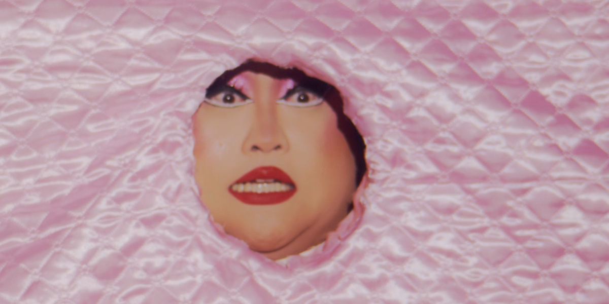 RuPaul's Drag Race 1704: A close up of Joella's face in a hole in a comforter.