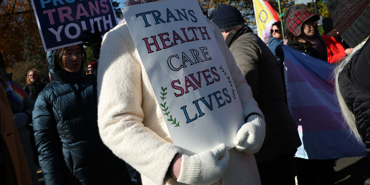 a person holding a sign that says TRANS HEALTH CARE SAVES LIVES at a gender-affirming care rally