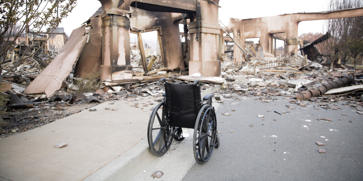 An abandoned wheelchair on a street facing destruction from a wildfire.