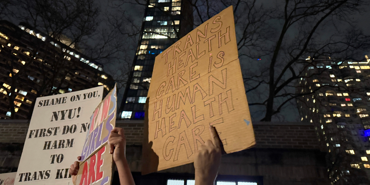 Hands hold up signs at the NYU Langone trans healthcare protest that read Trans Healthcare is human healthcare and shame on you NYU