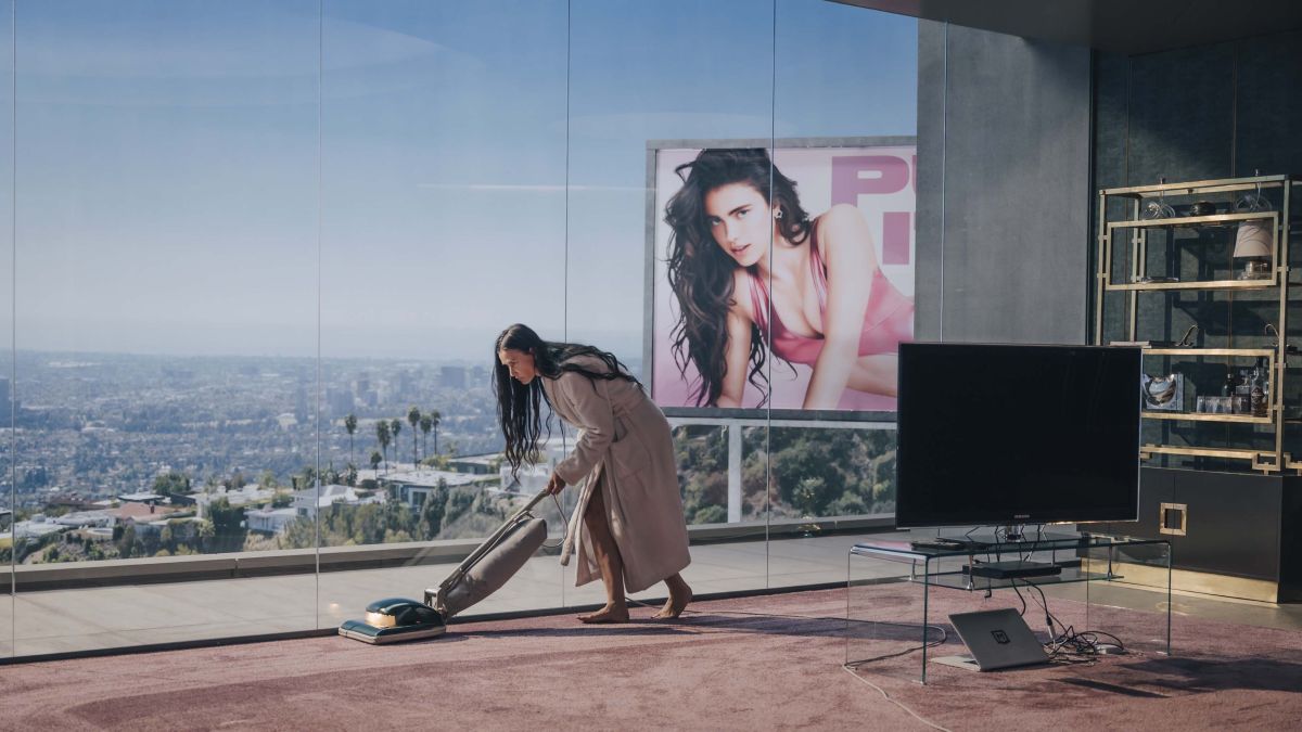 Demi Moore vacuums a minimalist apartment with a billboard of Margaret Qualley behind her.