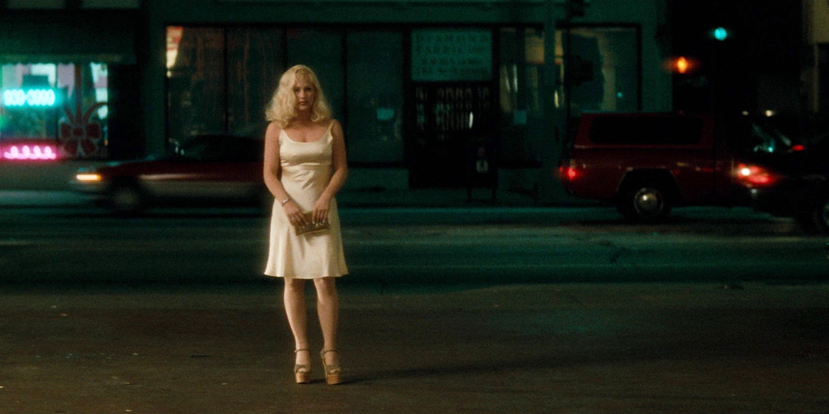 Sex work and David Lynch: Patricia Arquette in a white dress and a blonde wig stands in the street darkness around her.